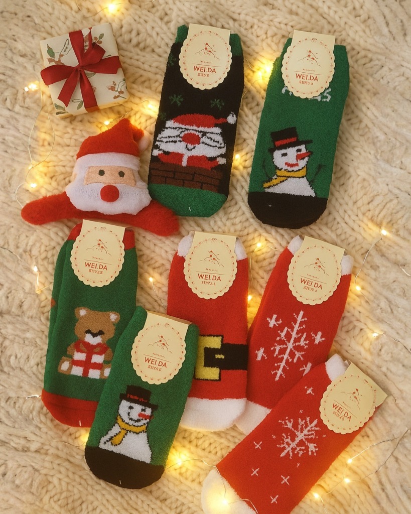 A collection of seven pairs of short Christmas socks for women or men, featuring assorted festive patterns including Santa, snowman, reindeer, bear, stripes, and snowflakes, displayed on a fluffy white surface.