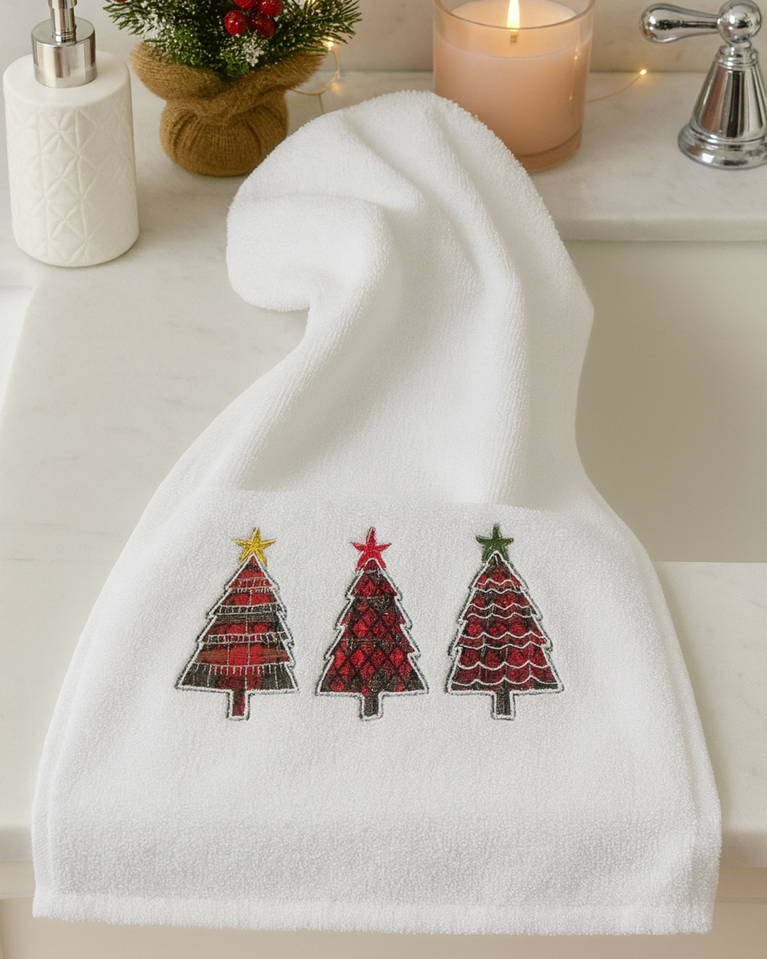 Embroidered Christmas hand towel (30x50 cm) displayed in a bathroom setting with festive ornaments, featuring red and black patterned Christmas trees on white fabric.