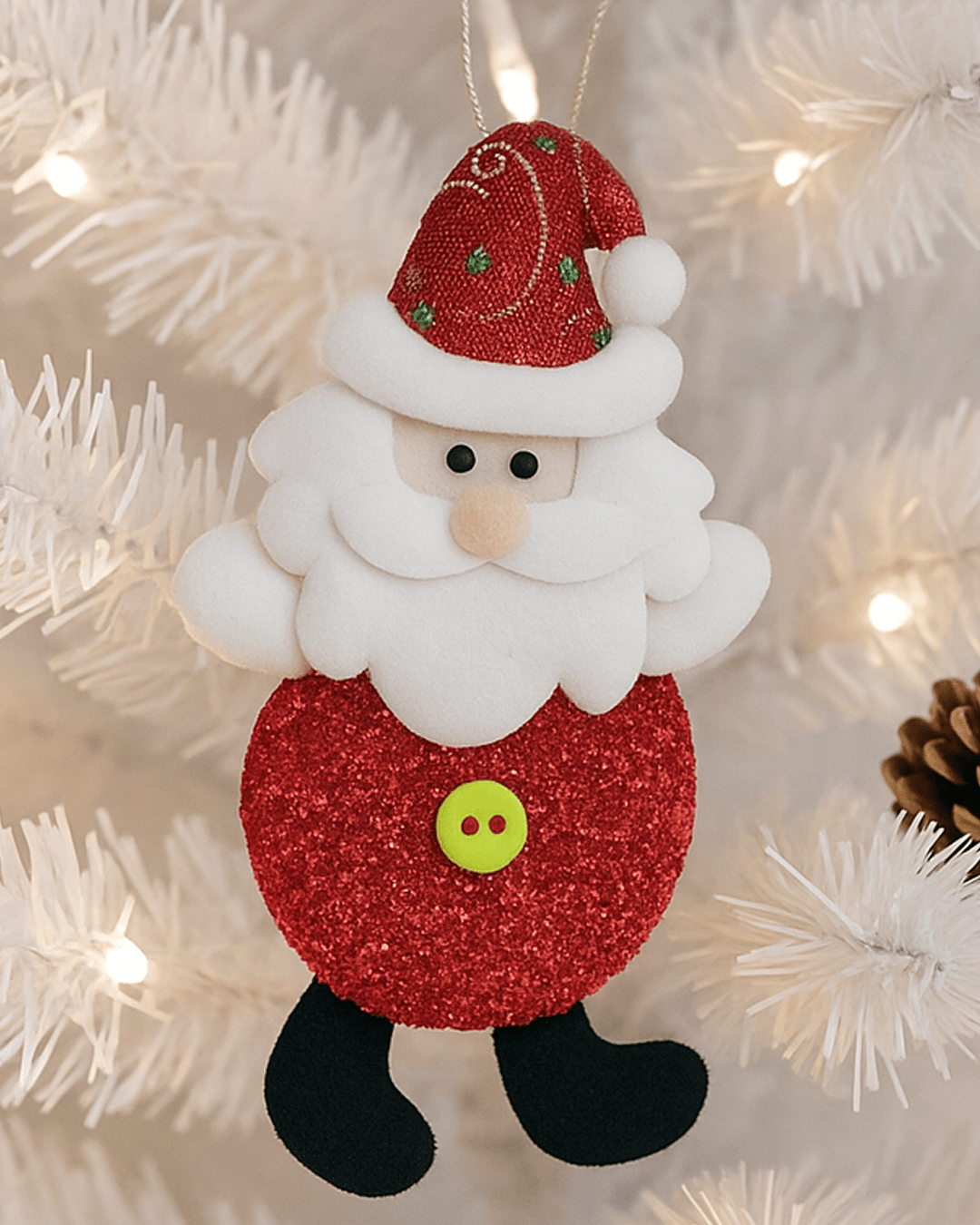 A close-up of two different handmade Santa Claus Christmas tree ornaments, one made of red felt with a snowflake and one made of red glitter fabric, both featuring soft white beards and hanging on a white pre-lit Christmas tree.