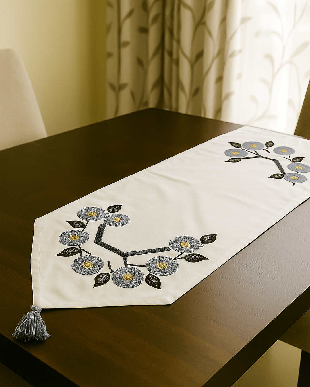 Floral embroidered table runner with blue punch-needle flowers and tassel ends on a wooden dining table.
